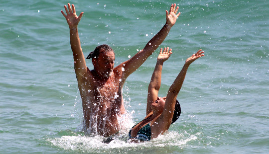 ,man and woman in the ocean with hands up in the air in joy