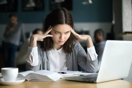 אישה צעירה בוהה במחשב הנייד שלה ומחזיקה את המוצאים שלה לראשה