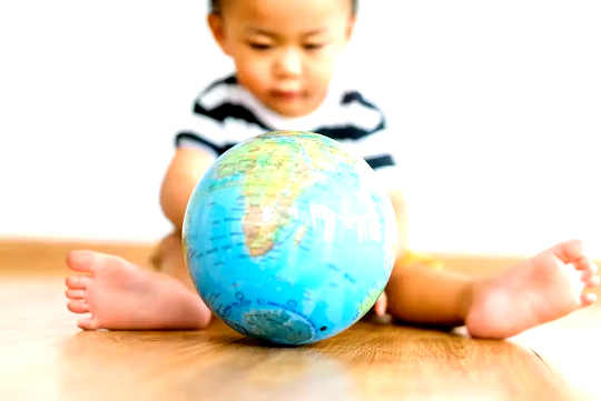 फर्श पर बैठा एक बच्चा विश्व ग्लोब के साथ खेल रहा है