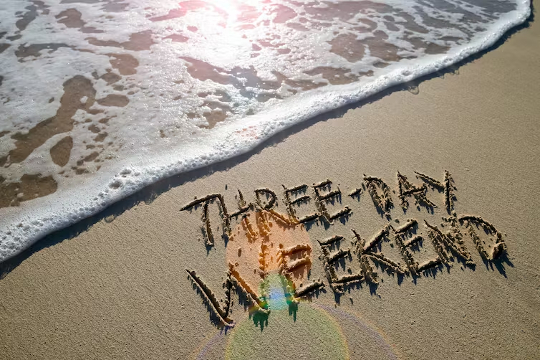 en strand med ordene "3-dages weekend" skrevet i sandet