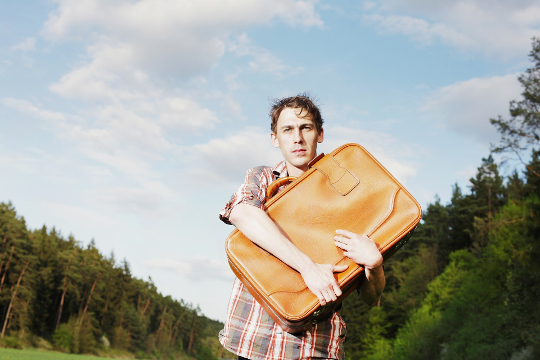 رجل يقف في الخارج ممسكًا بحقيبة سفر على صدره