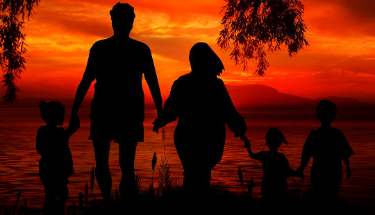 sebuah keluarga berpegangan tangan dan berdiri setinggi pergelangan kaki di dalam air