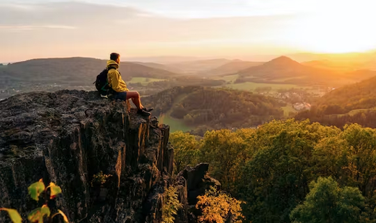 एक पर्वतारोही प्रकृति में चट्टानों की एक चौकी पर बैठा है