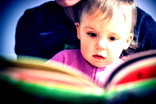 un bambino seduto sulle ginocchia di sua madre e che legge da un libro