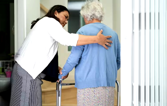 hoitaja, joka auttaa iäkkäämpää naista kävelemään