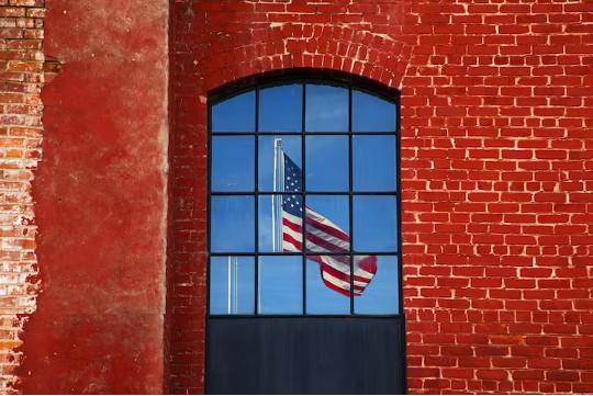 una bandera estadounidense vista a través de una ventana en una pared de ladrillo rojo