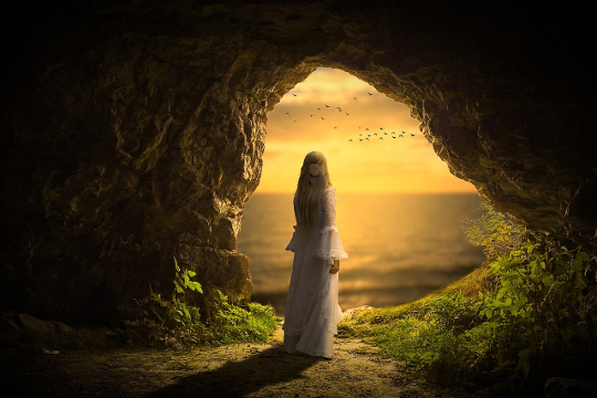 kobieta stojąca w ciemnej jaskini, patrząca w jasne niebo