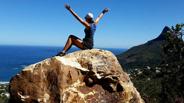 mujer sentada en la cima de una montaña con los brazos extendidos en señal de triunfo