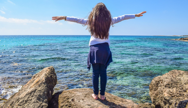 fată tânără cu brațele larg deschise în fața oceanului