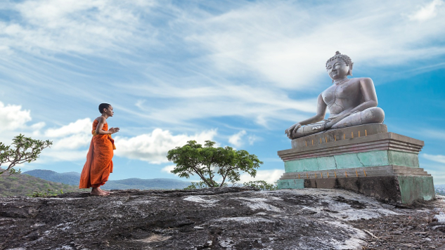 statue av buddha med en ung munk stående foran