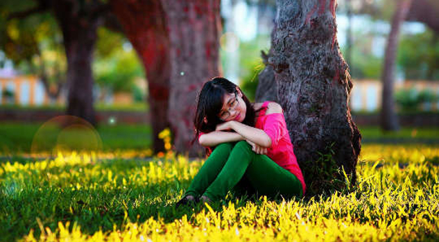 wanita muda duduk di bawah pokok dengan mata tertutup