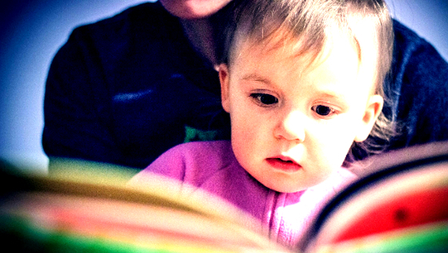 lille barn på skødet af en voksen, der ser på siderne i en farverig bog