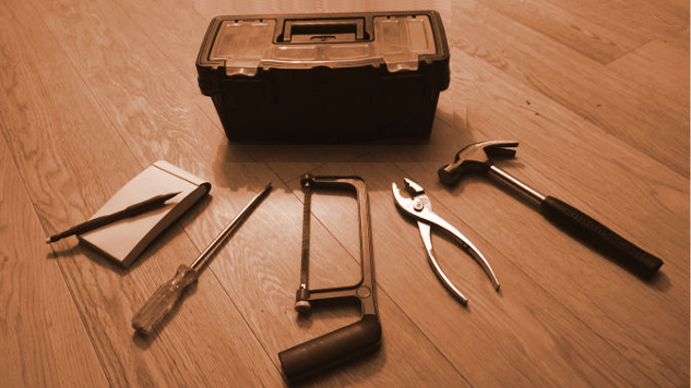 Takenbox met 5 gereedschappen eromheen verspreid: notitieblok, schroevendraaier, ijzerzaag, tang, hamer