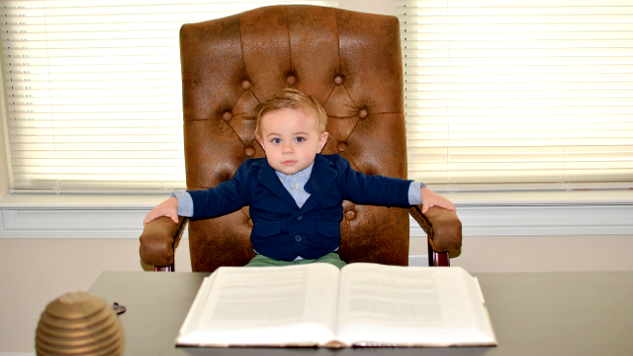 młody chłopak siedzi na dużym skórzanym krześle przed biurkiem biznesowym