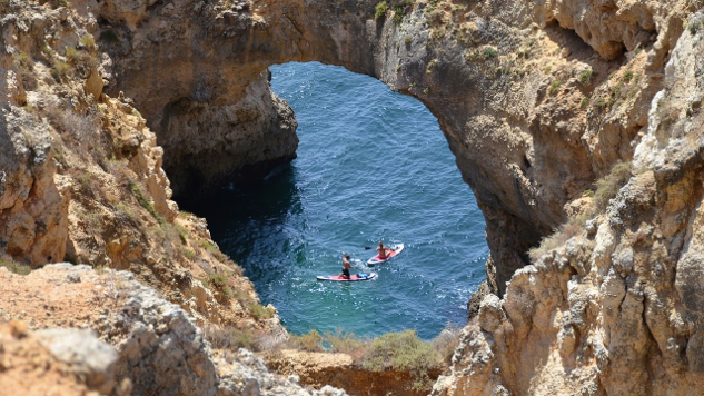 Dos kayaks en el agua pasando bajo un arco de piedra.