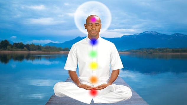 mężczyzna siedzący w medytacji z oświetlonymi czakrami
