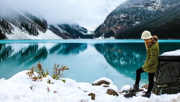 Mujer joven parada en la nieve junto a un lago.