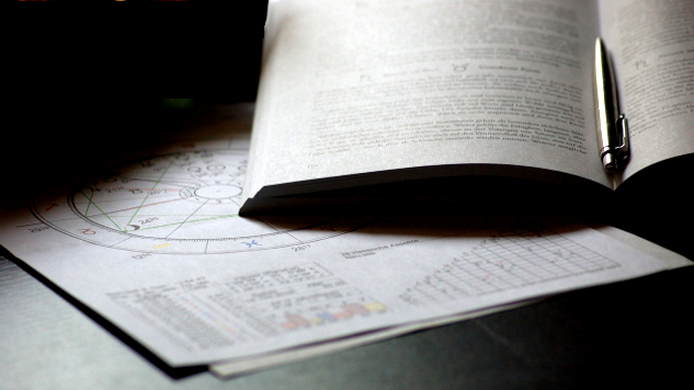 um mapa astrológico, um livro aberto e uma caneta