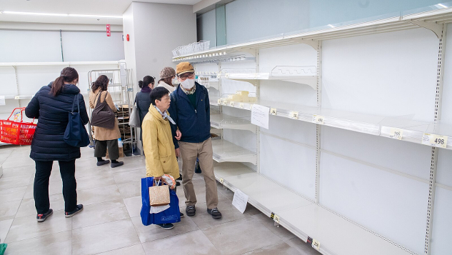 shoppare som bär Covid-masker framför tomma butikshyllor