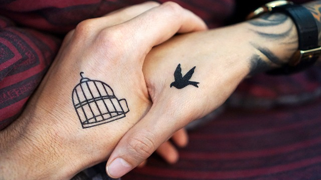 két összekulcsolt kéz... az egyiken nyitott madárketrec tetoválás, a másikon egy madár repül