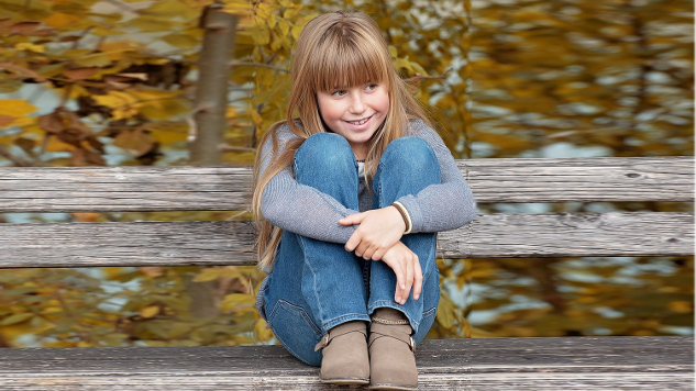 mosolygós fiatal lány kint ül egy padon