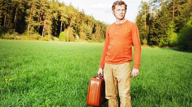 mies seisoo yksin piteleen matkalaukkua
