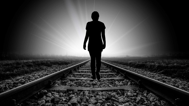 demiryolu hattında ışığa doğru yürüyen bir kişinin silueti