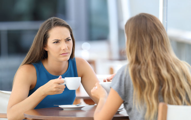 dua wanita menghadap antara satu sama lain sambil minum kopi