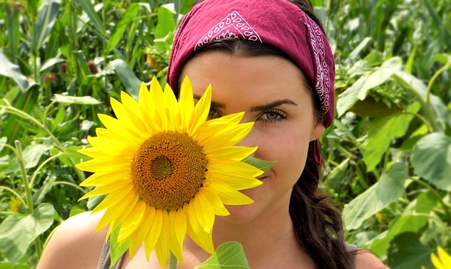 seorang wanita berdiri sedikit di belakang bunga matahari yang sebesar kepalanya