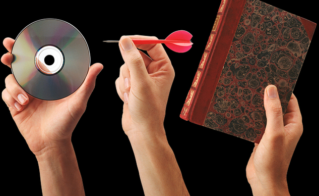 рука держит книгу, другая рука держит дротик, нацеленный на компакт-диск с отверстием в центре