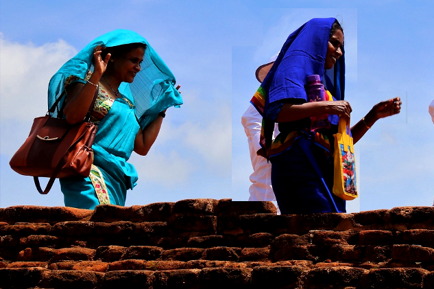 două femei care trec pe lângă un zid de cărămidă... una zâmbește larg