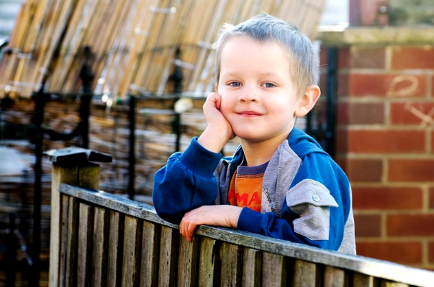 ένα νεαρό αγόρι που στέκεται σε έναν φράχτη και κοιτάζει ειρηνικά