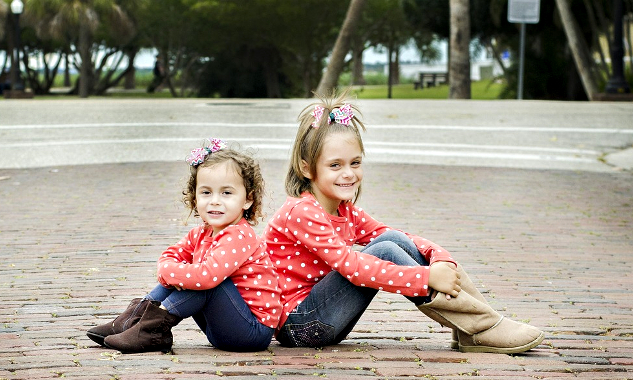 två leende unga systrar sitter rygg mot rygg