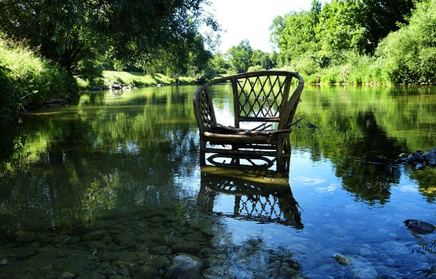 a wicker chair in the calm waters of a river near the riverbank