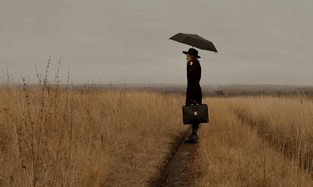image d'une femme sur un sentier dans un champ ouvert et tenant une valise