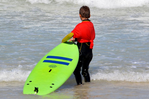 Kind steht am Rande des Ozeans und hält ein Body-Surfbrett