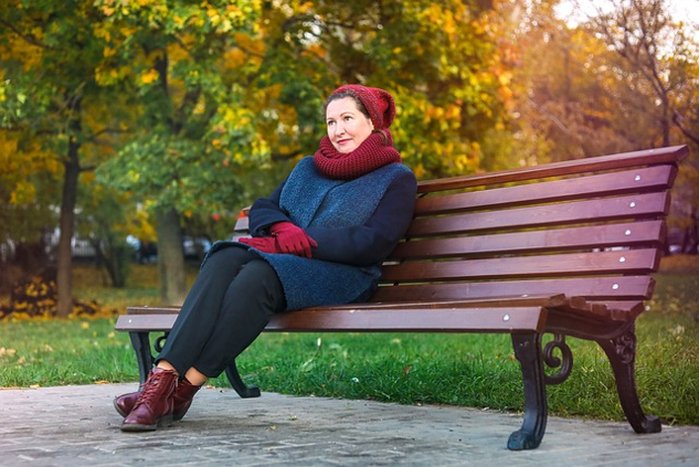 शरद ऋतु के दिन पार्क की बेंच पर बैठी मुस्कुराती हुई महिला