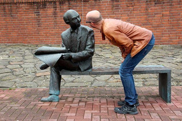 un homme se penchant pour regarder de près une sculpture sur un banc