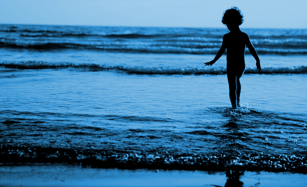 युवा लड़का पानी में उठती लहरों के किनारे खड़ा है