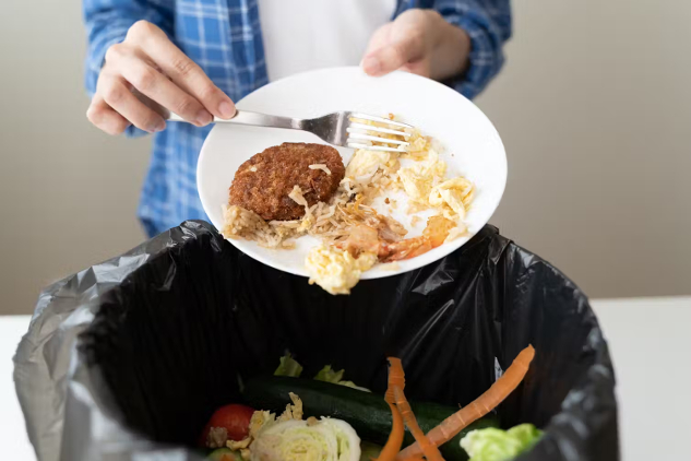 Bir kişi atık yiyecekleri çöp kutusuna döküyor.