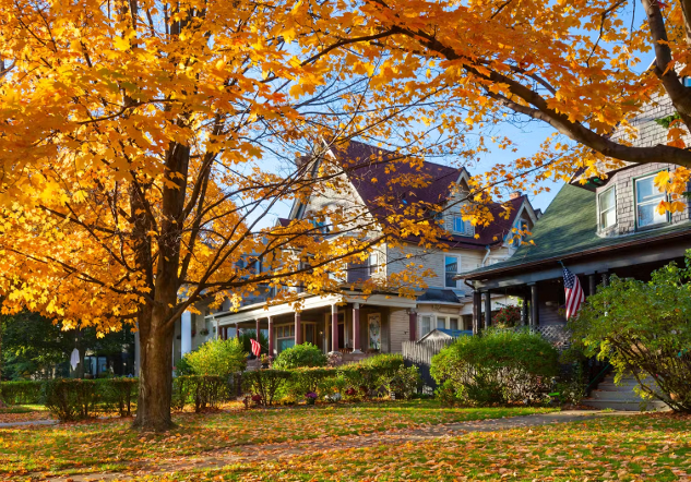 Zwei historische Häuser im Herbst, deren Vorgärten mit orangefarbenen Blättern bedeckt sind.
