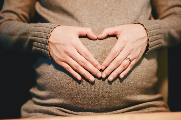 De handen van de vrouw vormen een hartvorm bovenop haar baarmoeder