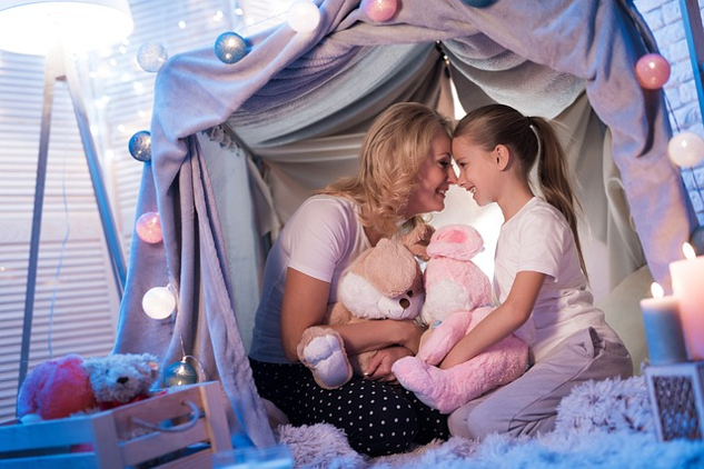mother and daughter sitting happily in a "fort" made from sheets
