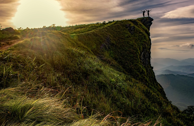 two people standing triumphantly on the edge of a cliff