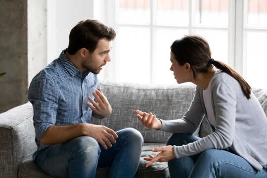 Uma mulher e um homem discutem sentados em um sofá.