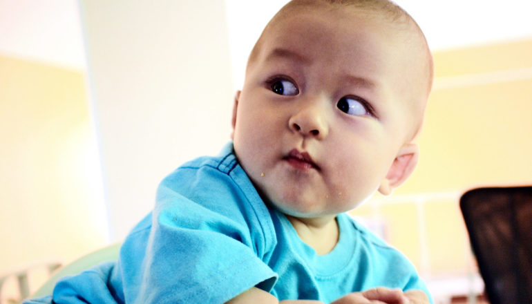 Seorang bayi dengan baju biru kelihatan di atas bahunya dengan mata yang luas