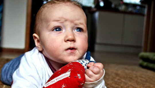 Un bébé sur le sol lève les yeux avec un front plissé