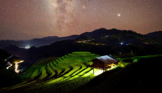 küçük binanın altından gelen parlak ışık yıldızlı gökyüzünün altında teraslı pirinç tarlaları