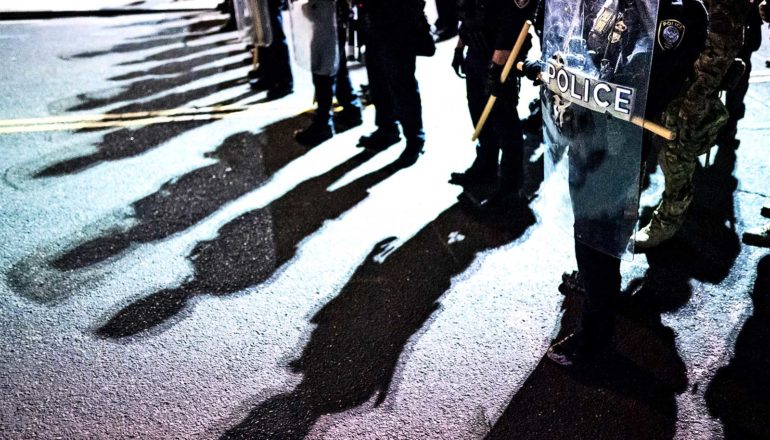 En række politi med oprørskærme på gaden kaster skygger på asfalten