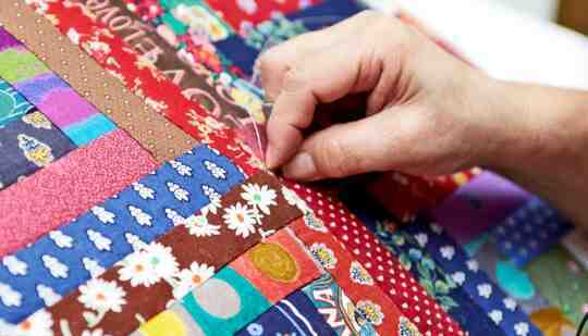 Una persona cose una colcha de diferentes piezas de tela.